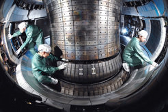 Installation work in the plasma vessel. The collector plates of the divertor are seen at the bottom. The transformer coil is located behind the middle column. The plasma vessel is surrounded by the main and vertical-field coils.