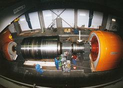 Einer der Schwungrad-Generatoren im IPP: Links das große Schwungrad, unter der Haube rechts der Generator. An der mit Pfeil markierten Stelle auf der Achse misst ein Sensor die Drehschwingungen.
