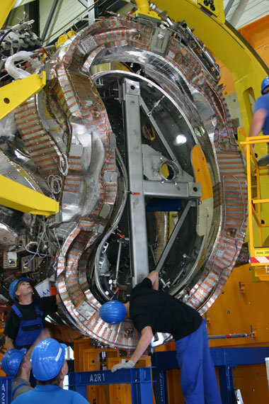 <p>Aus den Rechnungen der Plasmaphysiker und Konstrukteure sind fertige Spulen geworden, hier beim Auffädeln auf das Plasmagefäß</p>