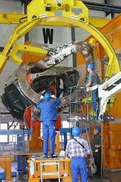 The first step in assembling the Wendelstein 7-X fusion device at Greifswald: Suspended in a rotatable support structure, the first of 50 stellarator magnet coils is strung onto a segment of the plasma vessel.