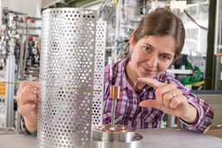 Dr Eve Stenson uses spare parts to demonstrate the structure of the prototype trap: in the centre is the permanent magnet, the wire on the left represents a probe that can be inserted into the trap. It allows researchers to determine the quantity of injected particles successfully captured inside the magnetic field.