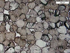 A sample of the tungsten heavy alloy HPM 1850 after polishing and etching. It shows individual grains of tungsten, which are etched slightly differently according to their grain orientation. The light grey areas between the grains represent the nickel-iron alloy matrix. The scale bar in the top right corner is 100 µm, i.e. 0.1 millimetres.