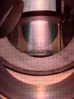 Blick ins Innere der Plasmaquelle "PlaQ“ während des Plasmabetriebs. Im oberen Teil ist der "Käfig" erkennbar. Der aus dem Käfig austretende Plasmastrahl trifft unten auf den Probenhalter.